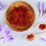Bunch of saffron stamens, crocus buds, in a wooden plate and spoon on a white background. The most expensive spice.
