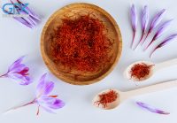 Bunch of saffron stamens, crocus buds, in a wooden plate and spoon on a white background. The most expensive spice.