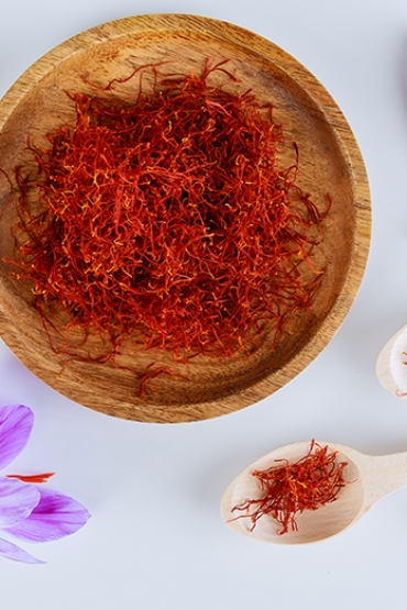 Bunch of saffron stamens, crocus buds, in a wooden plate and spoon on a white background. The most expensive spice.