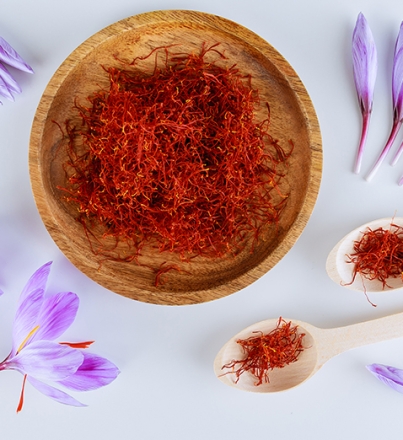 Bunch of saffron stamens, crocus buds, in a wooden plate and spoon on a white background. The most expensive spice.